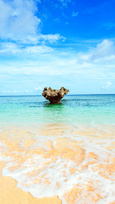 沖縄を連想させる美しい砂浜で真ん中に大きなオブジェのような岩がある写真
